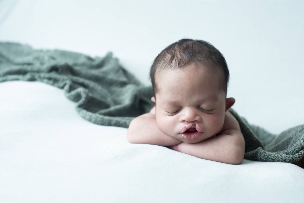 Newborn Yonas sleeping peacefully with his chin resting on his hands, wrapped in a sage green knit blanket