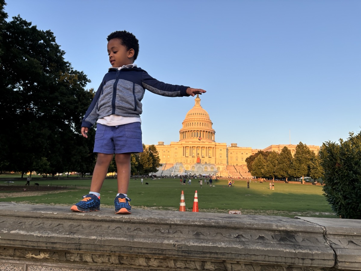 Yonas walking along a stone wall at golden hour with the U.S. Capitol building glowing in the background