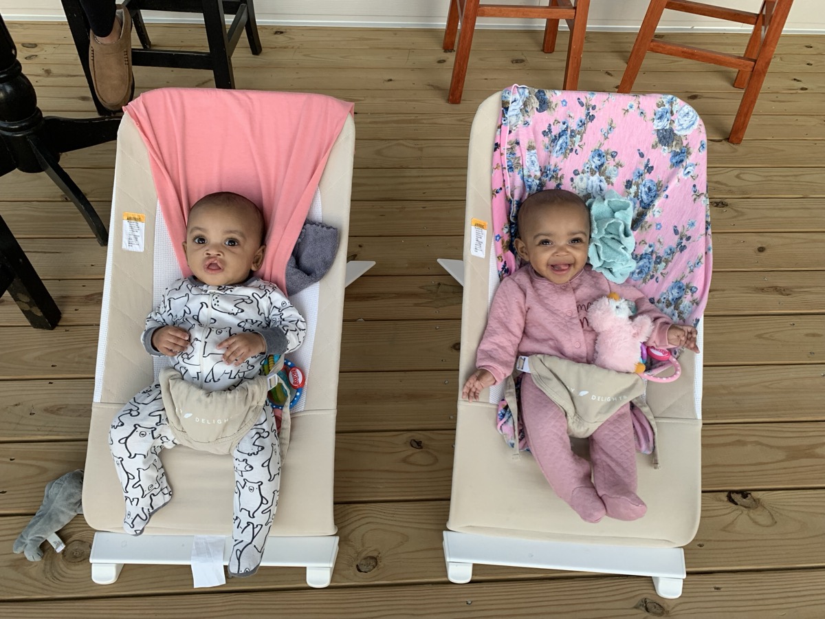 Baby Yonas and his twin sister side by side in matching bouncer seats, Yonas in a white bear-print onesie and his sister smiling in pink