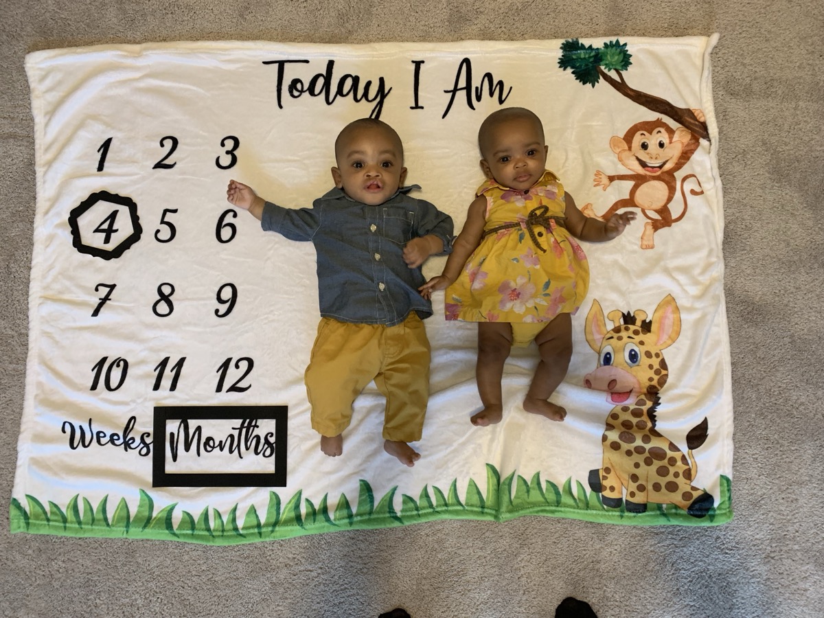 Yonas and his twin sister on a milestone blanket marking 4 months, Yonas in a denim shirt and khaki pants with jungle animal decorations