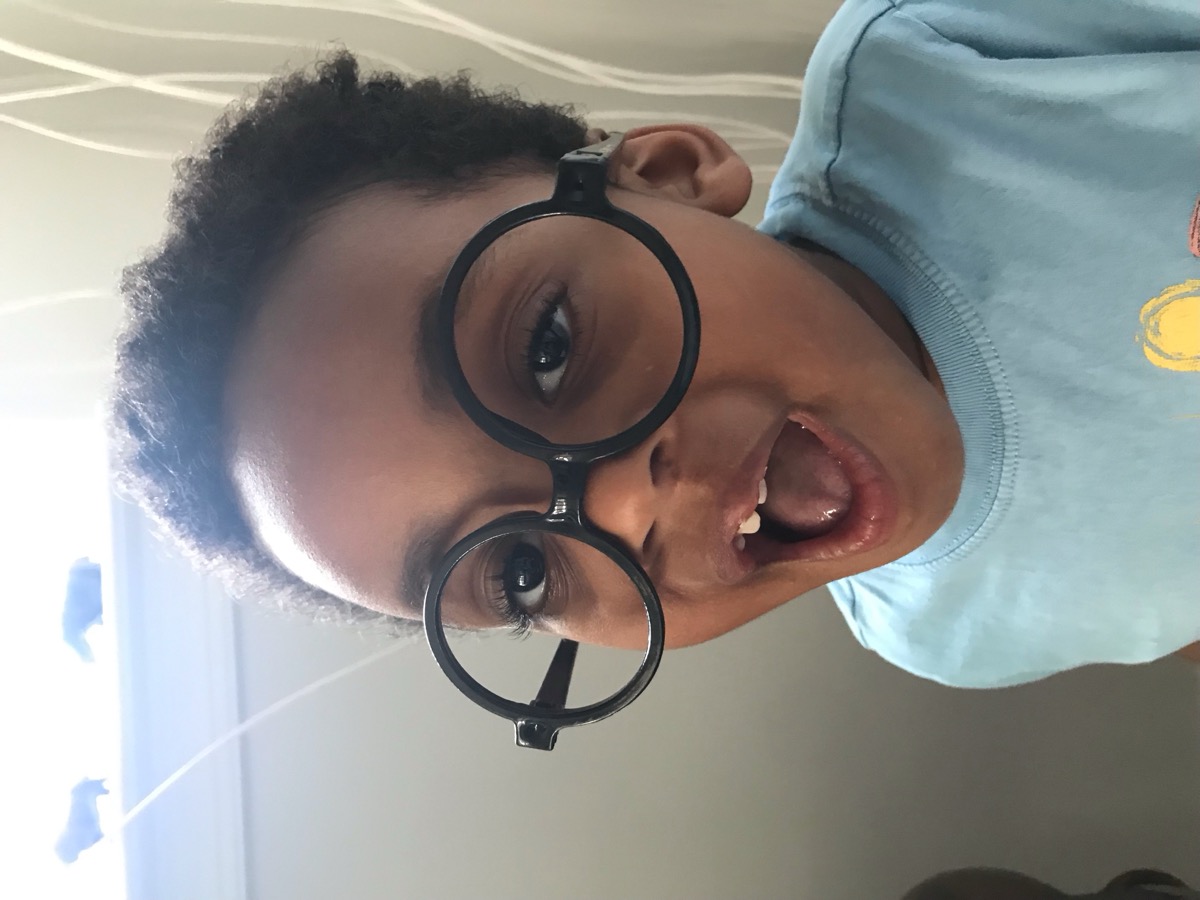 Close-up of Yonas with curly hair making a silly face wearing oversized round black costume glasses and a light blue shirt