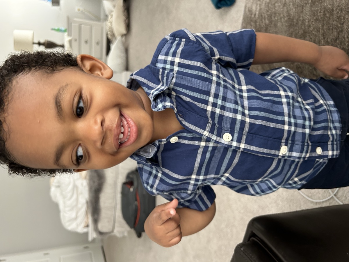 Yonas looking happy in a navy and white plaid button-down shirt with curly hair, smiling in the bedroom