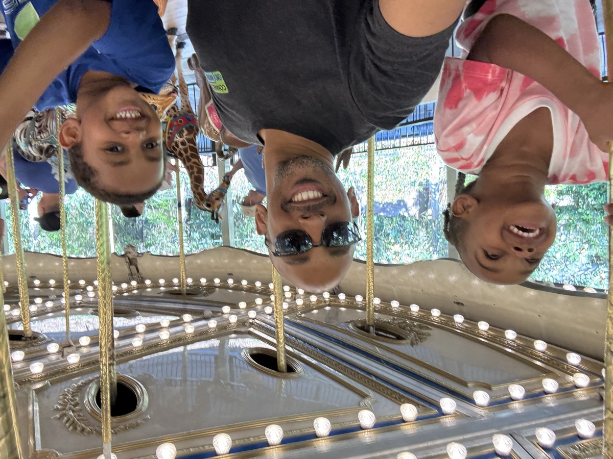 Yonas, his twin sister, and their dad on a carousel ride at the zoo, everyone smiling big with decorative lights above