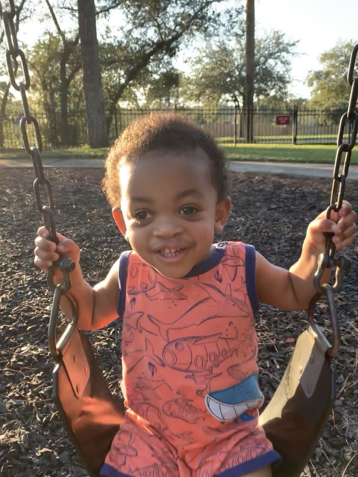 Yonas running on a playground in sneakers, wearing a graphic tee and shorts, curly hair bouncing as he plays