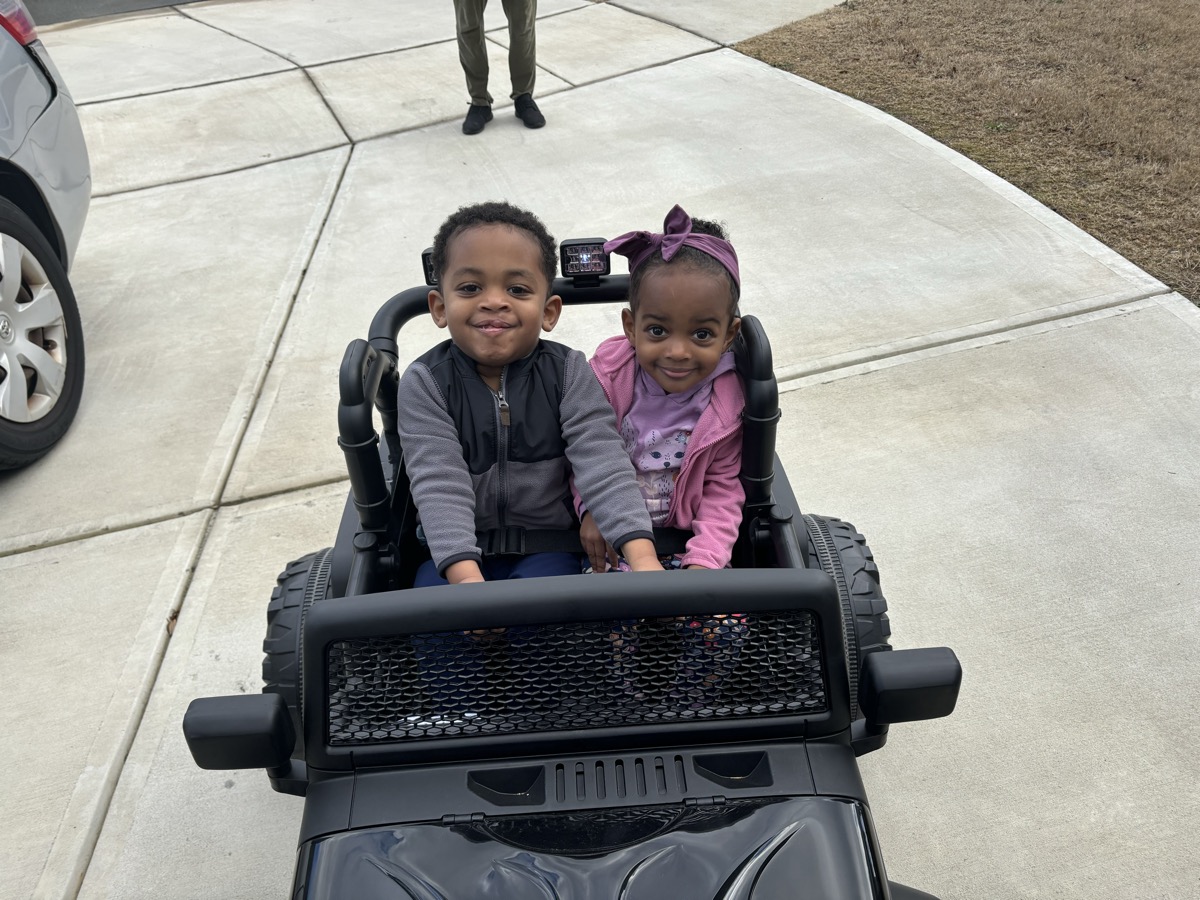 Yonas and his twin sister on a swing set, Yonas pumping his legs and laughing, mid-swing in the sunshine